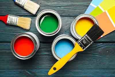 top view of different colours of paint in cans on a table with paint brushes and a colour chart
