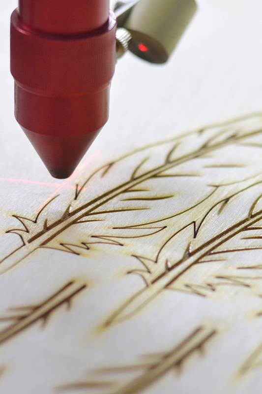 Laser Engraving machine over wood creating a tree pattern