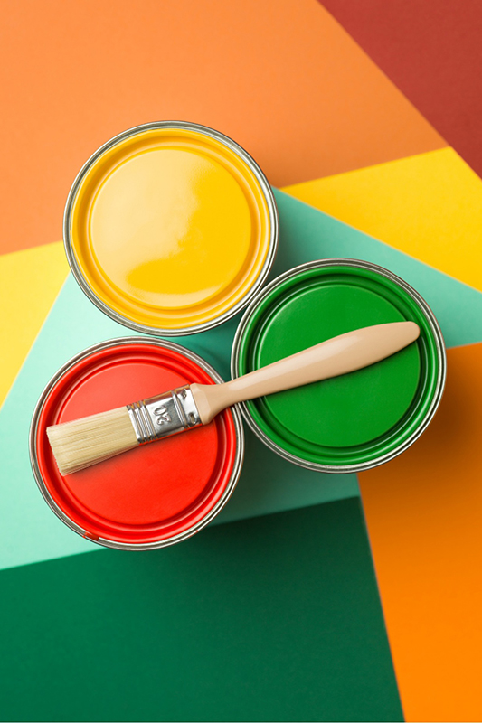 3 cans of paint in different colours with a paint brush on top on a coloured background