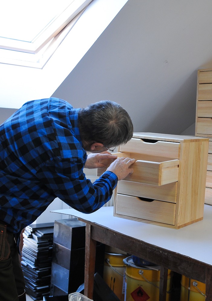 man in a blue checked shirt inspecting a wooden box on a table