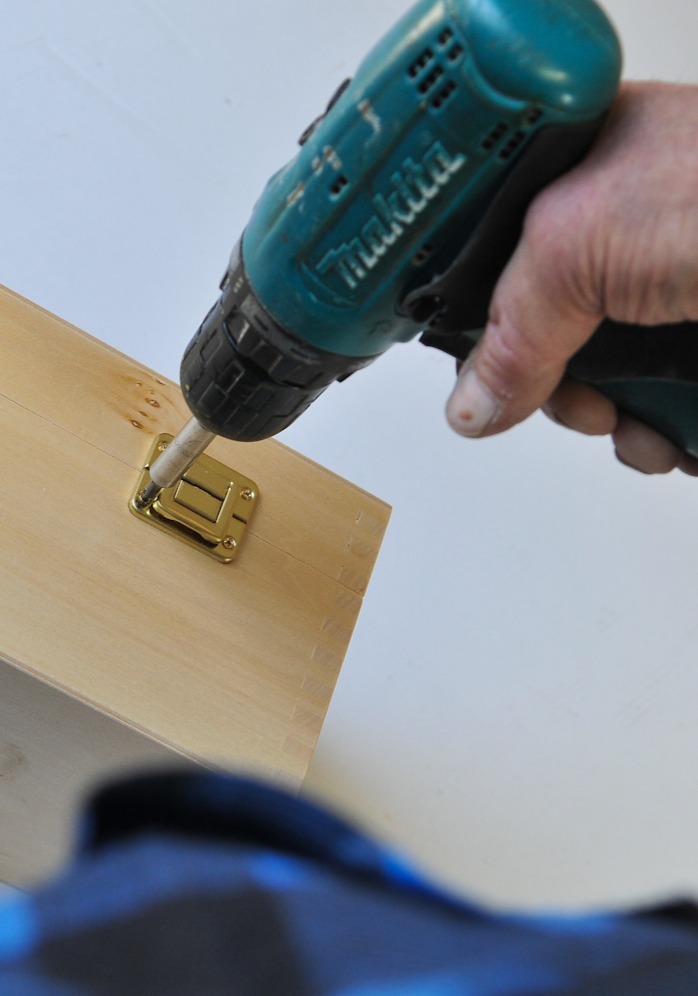 man holding a drill and attaching a metal clasp to a wooden box