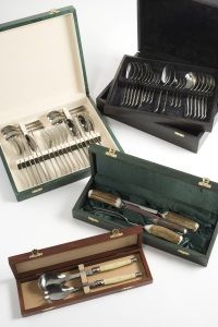 Four elegant cutlery sets are displayed in open cases on a white surface. Each set contains polished utensils neatly arranged, conveying sophistication.