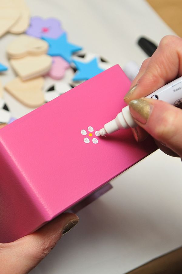 a person using a white marker printing a design on a pink wooden box