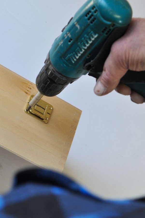 man holding a drill and attaching a metal clasp to a wooden box