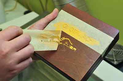 a hand pulling some tape off a box after it has been laser etched