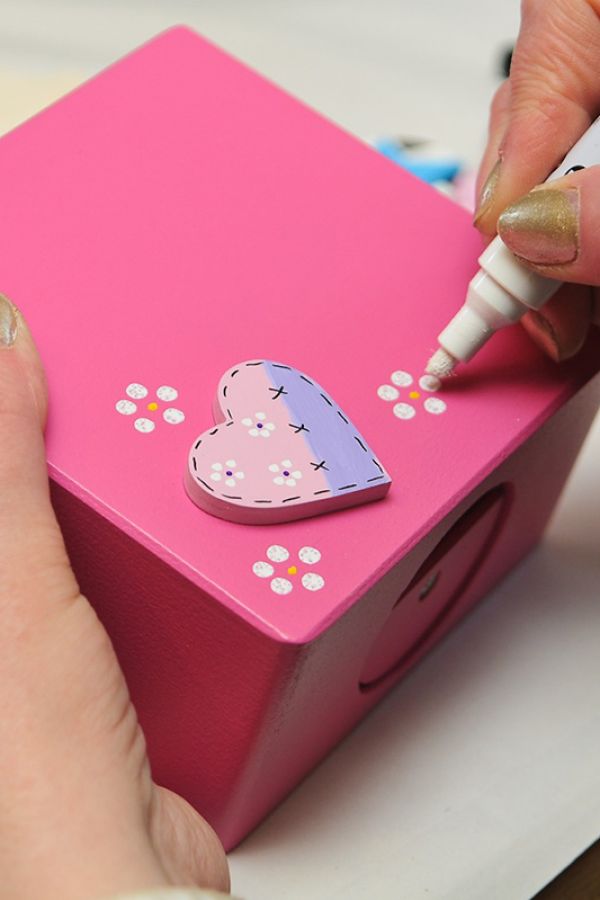 personn drawiing with a mamer pen on aa pink wooden box