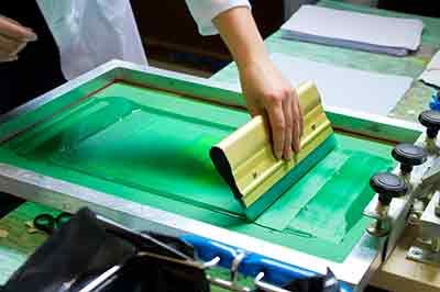 a persons hand with a squegee doing screen printing