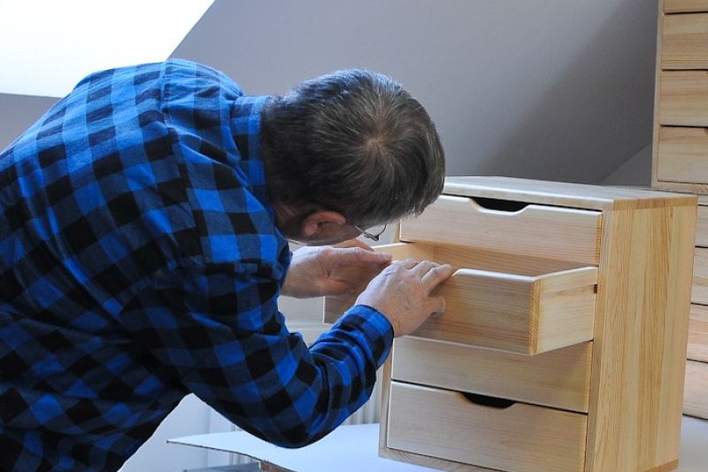 man in a blue checked shirt inspecting a wooden box on a table